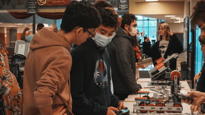 This image consists of four different photos. The first shows two team members working on their robot. The second shows the team leader, Sean, smiling. The third shows two team members running away from a pair of people in shark Halloween costumes. The fourth shows the first robot the Sileo team built.