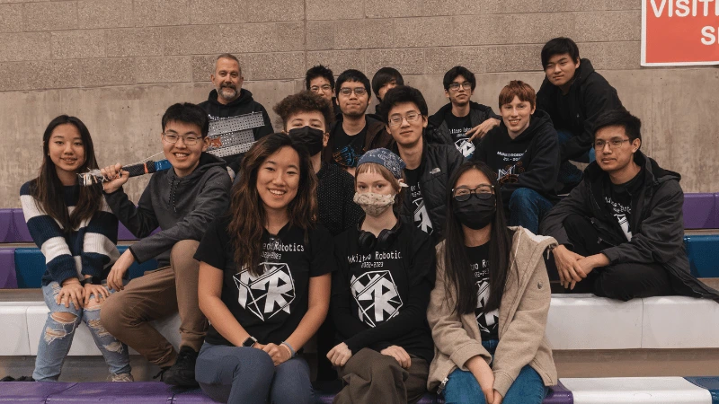 This image consists of four different photos. The first shows two teammates smiling next to the robot they built. The second shows a group of people working on one robot. The third shows a robot in its transport container. The fourth shows the middle school team competing at a League Day.